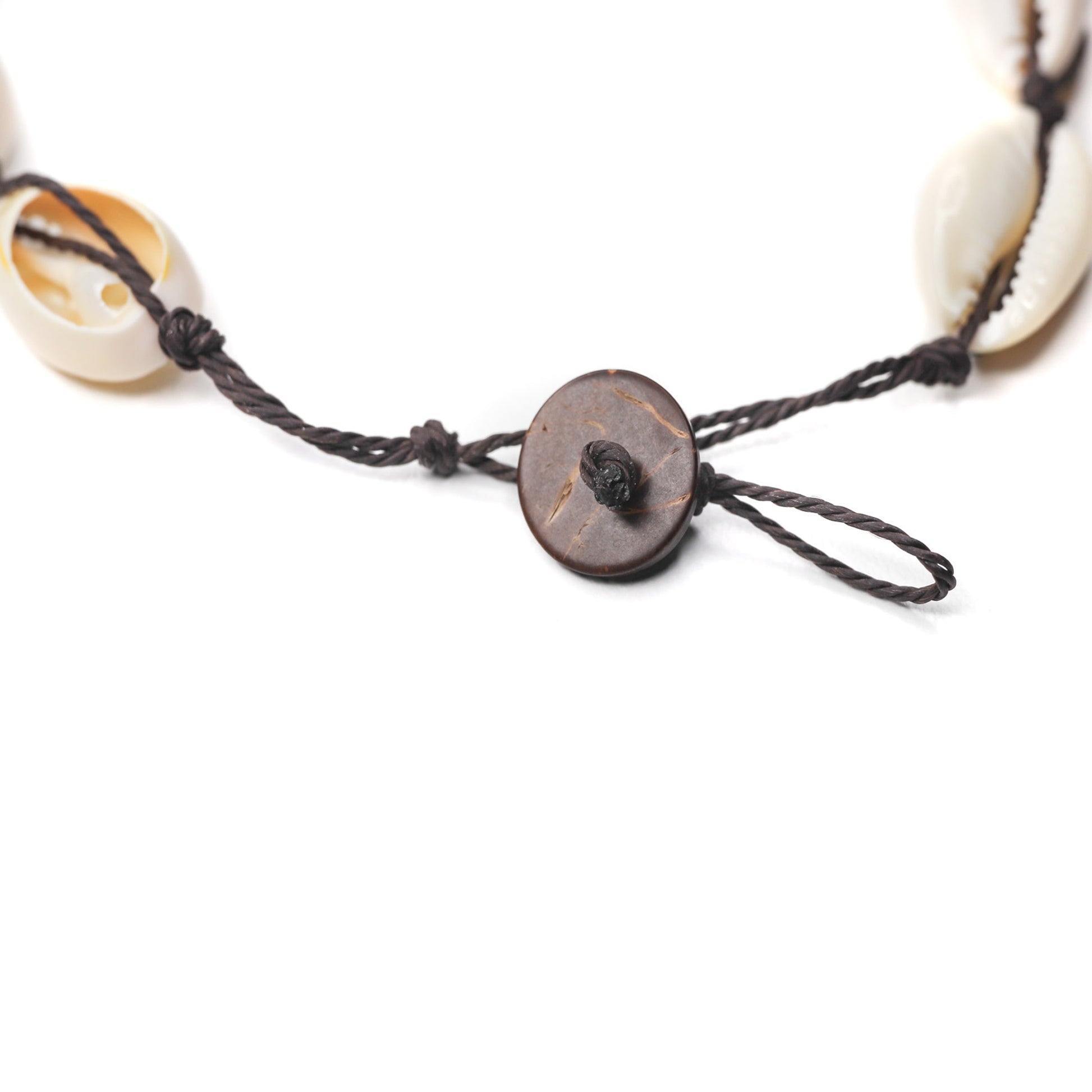 A close up of a cowrie shell choker adjustable coconut bead clasp.